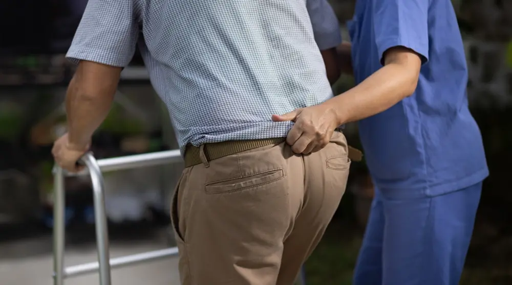 Idoso recebendo auxílio de enfermeira enquanto tenta se mover