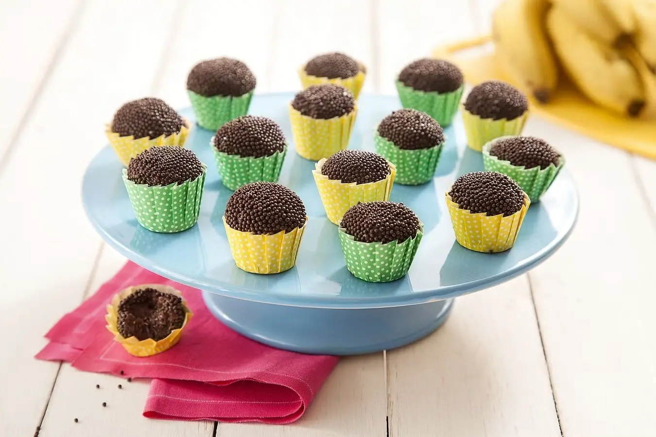 Foto de docinhos de festa decorados com chocolate granulado, dispostos em uma bandeja azul com cápsulas coloridas. Ótimo para comemorações e festas infantis.