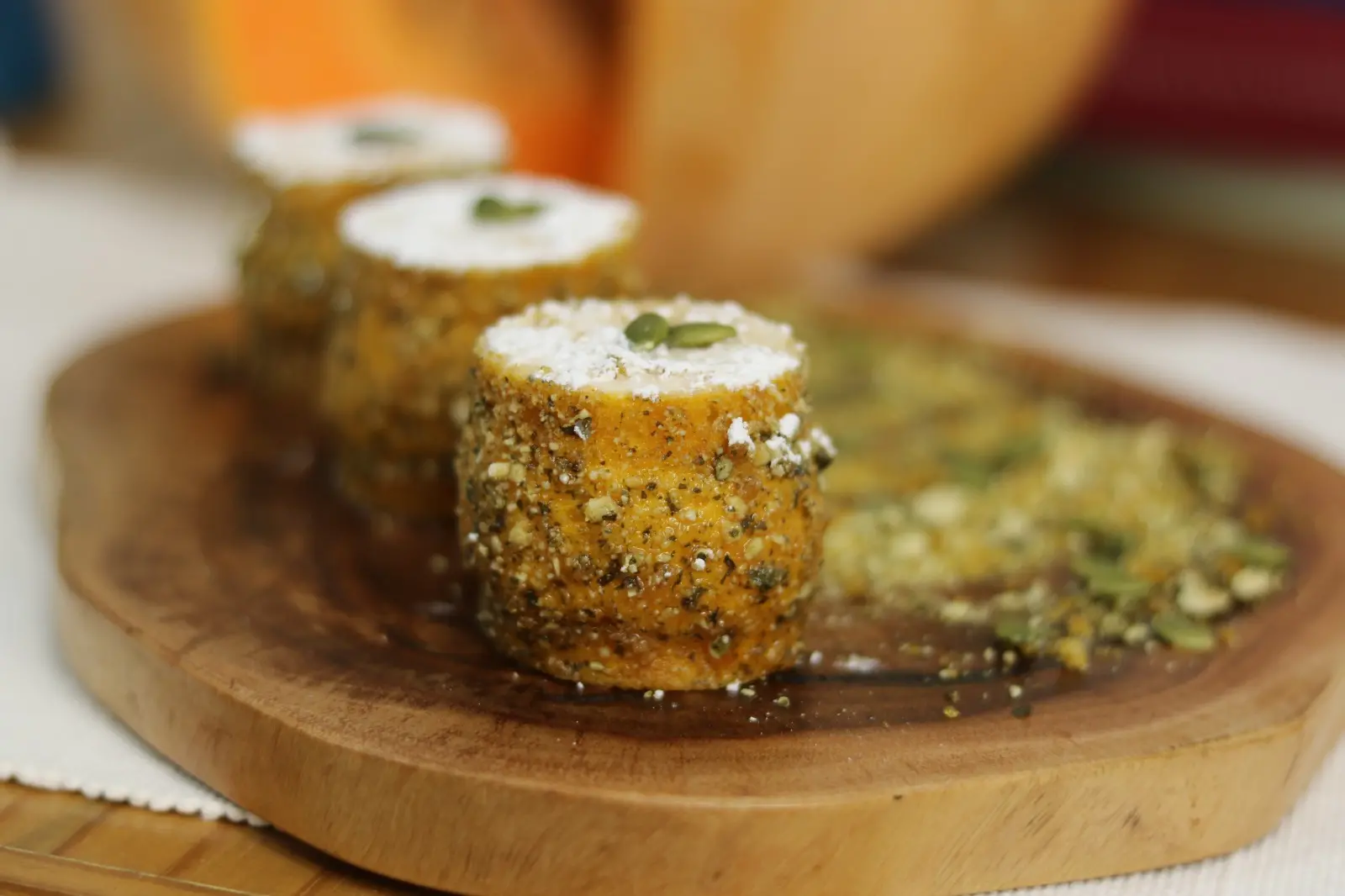 Imagem de pratos de alimentos empanados com recheios cream cheese, decorados com sementes e especiarias, dispostos sobre uma tábua de madeira para servir petiscos.