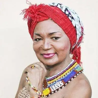 Thina Rodrigues, mulher negra com turbante vermelho e colares coloridos olha para a câmera com expressão serena