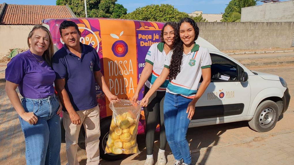 Quatro pessoas sorridentes ao lado de um carro de entrega de alimentos, promovendo a campanha de doação de alimentos, com destaque para a mensagem 'Nossa Popa' e uma sacola cheia de maracujás
