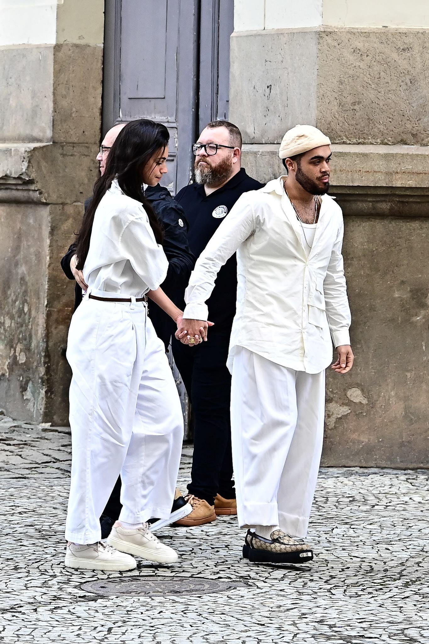 Casal segurando as mãos na rua, com um policial ao fundo, em uma cena de manifestação. Moda urbana, diversidade e protesto na cidade.