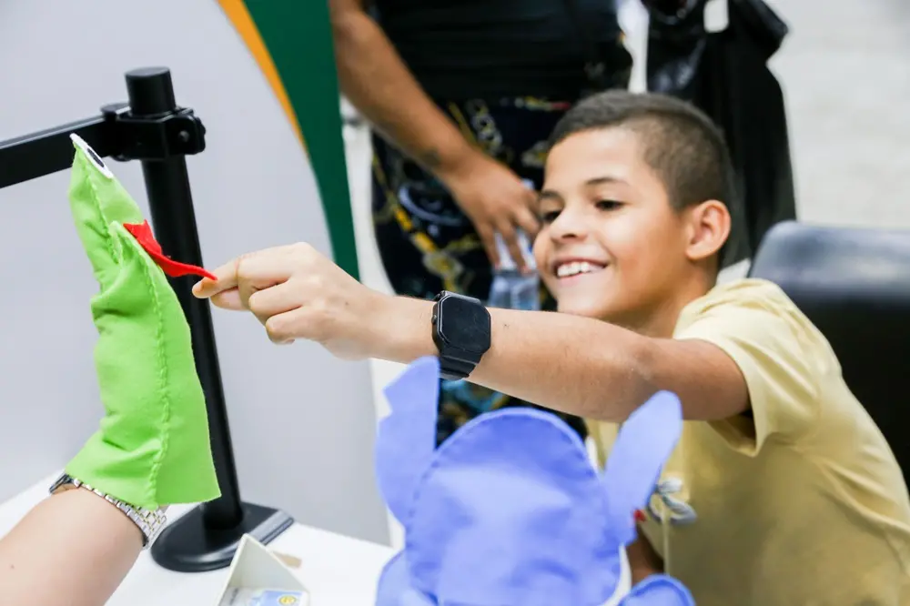 Na imagem, criança interage com fantoche desenvolvido por funcionária do Vapt Vupt Fortaleza durante atendimento