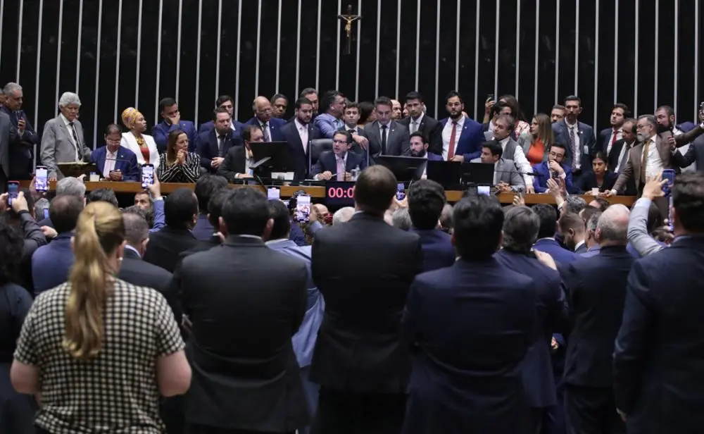 Deputados observam Hugo Motta, na Mesa Diretora da Câmara, fazendo pronunciamento