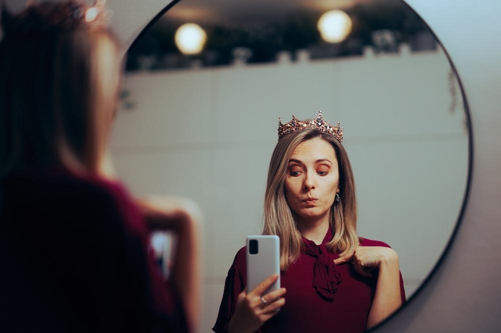 Na imagem, mulher olha para o espelho imaginando-se uma princesa, em alusão à trend 