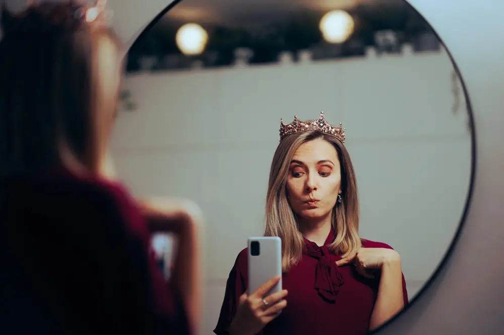 Na imagem, mulher olha para o espelho imaginando-se uma princesa, em alusão à trend 