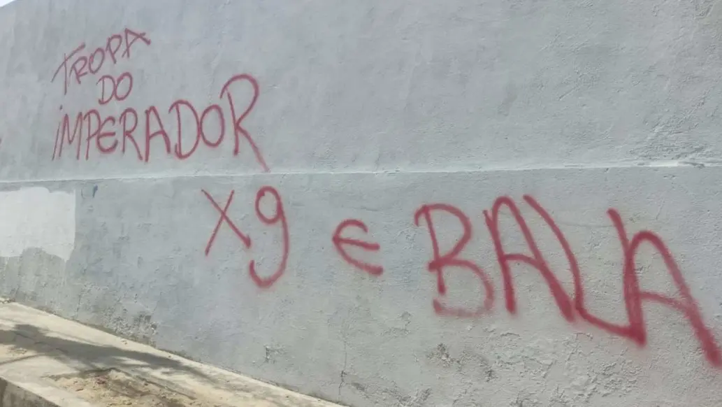 Foto mostra um muro branco pichado por uma facção criminosa, que se denomina Tropa do Imperador. Também foi pichada a ameaça 'X9 é bala'