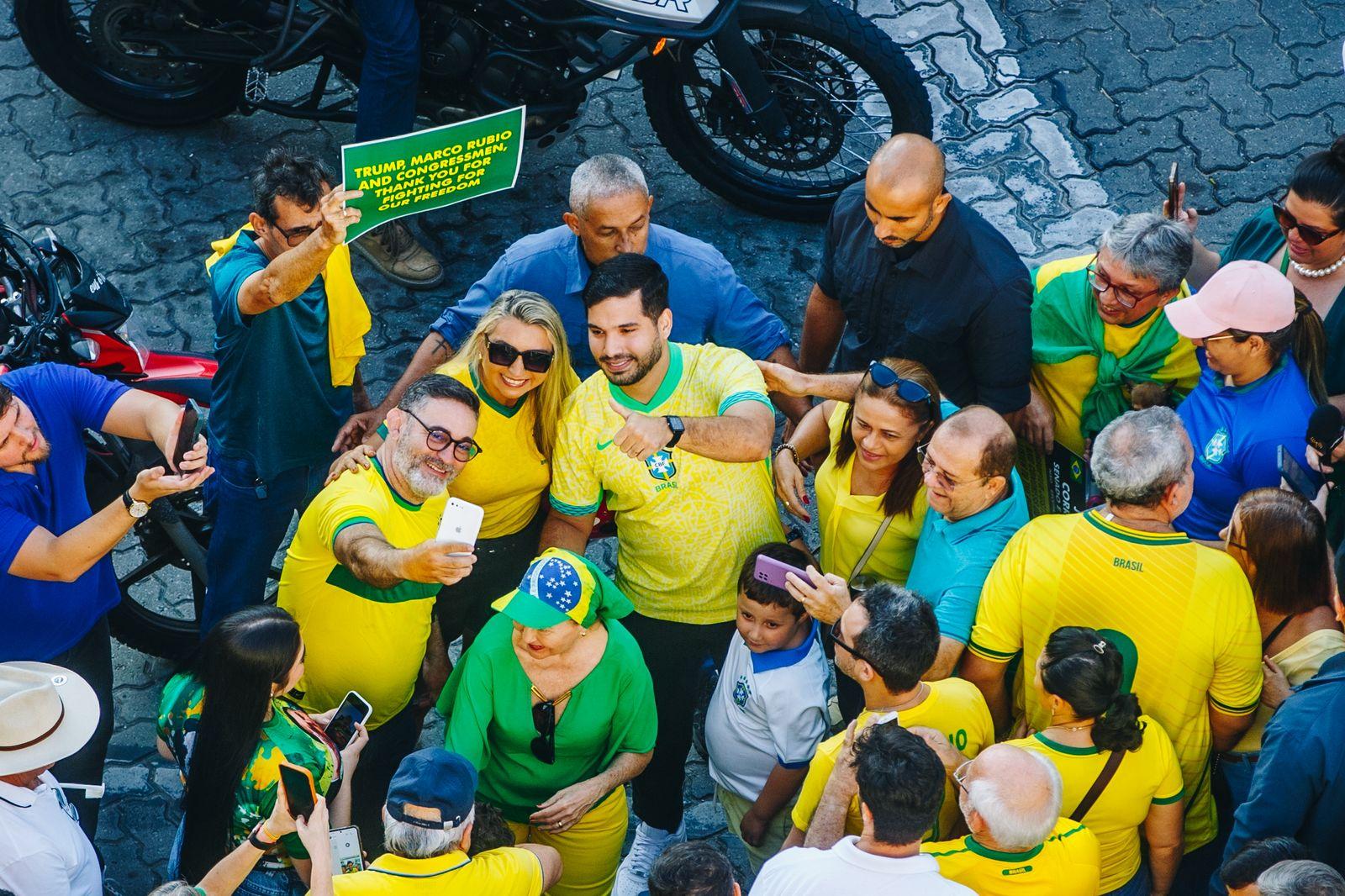 Foto de um grupo de pessoas em uma manifestação, muitas vestindo camisetas amarelas e verdes do Brasil. Elas estão posando para uma selfie no meio de uma multidão.