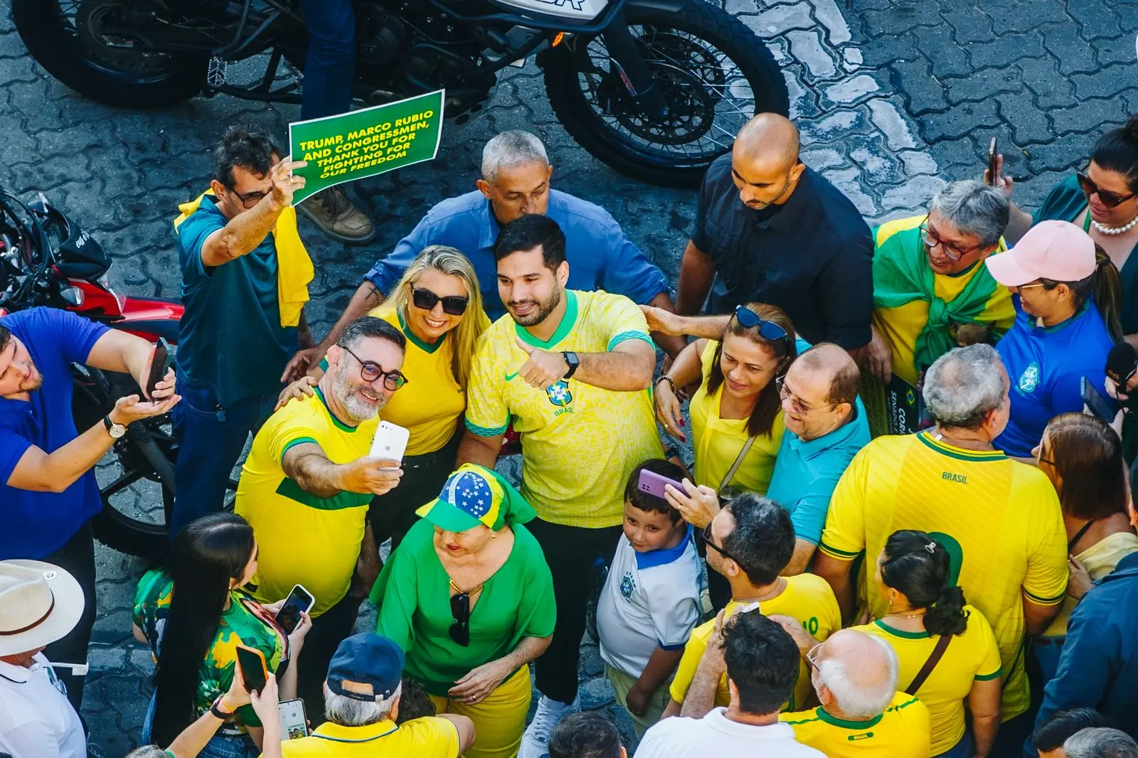 Foto de um grupo de pessoas em uma manifestação, muitas vestindo camisetas amarelas e verdes do Brasil. Elas estão posando para uma selfie no meio de uma multidão.