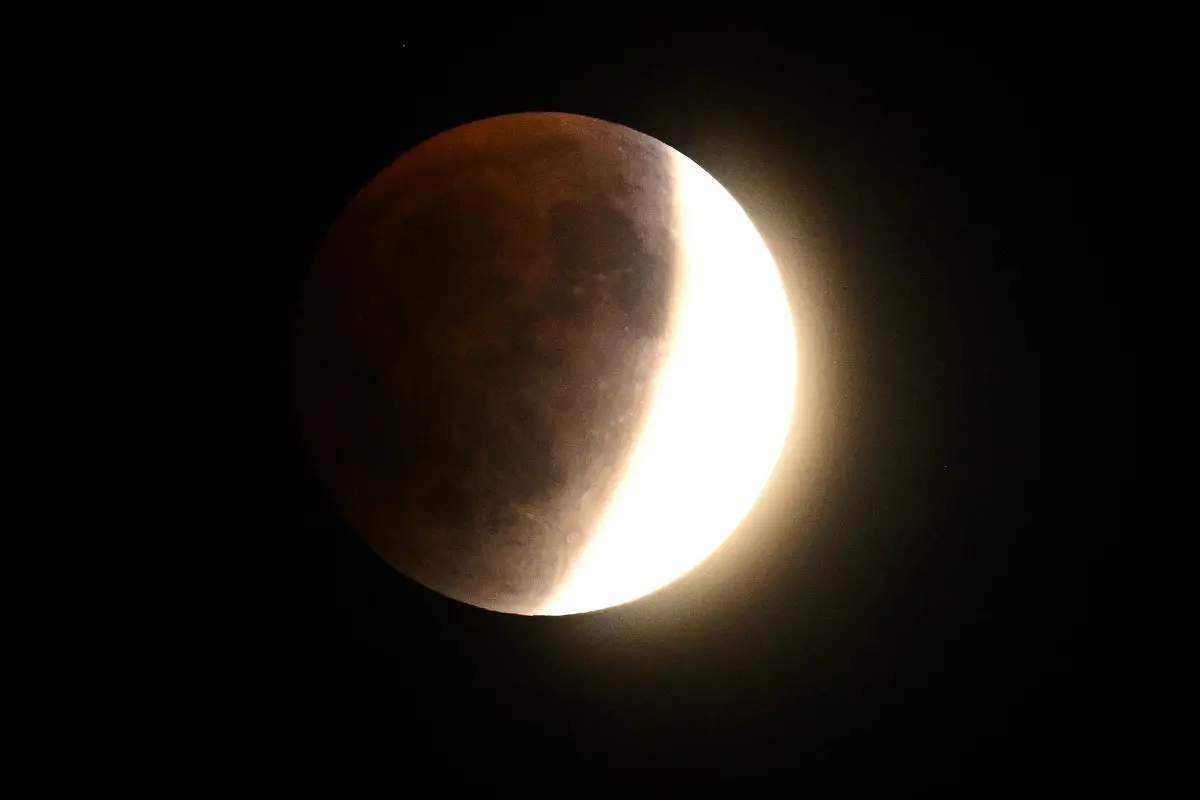 Imagem de uma lua durante um eclipse lunar parcial, mostrando a fase de penumbra com detalhes visíveis na superfície lunar, fundo preto.