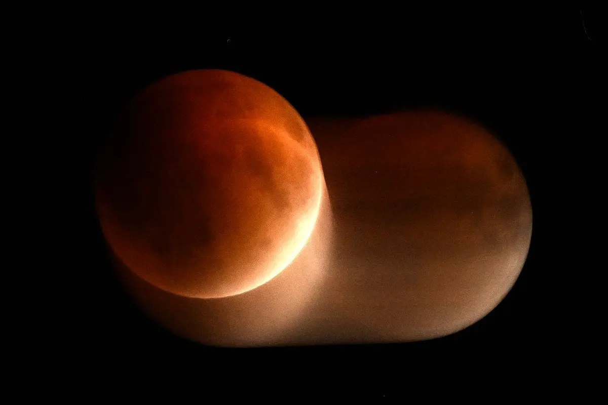 Imagem de um eclipse lunar com a lua parcialmente coberta por uma sombra avermelhada, criando um efeito dramático no céu escuro.