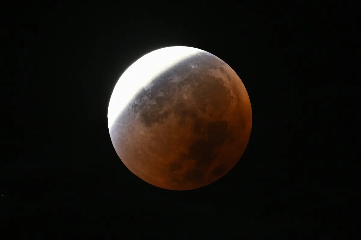 Imagem de um eclipse lunar com a lua parcialmente coberta por uma sombra avermelhada, criando um efeito dramático no céu escuro.