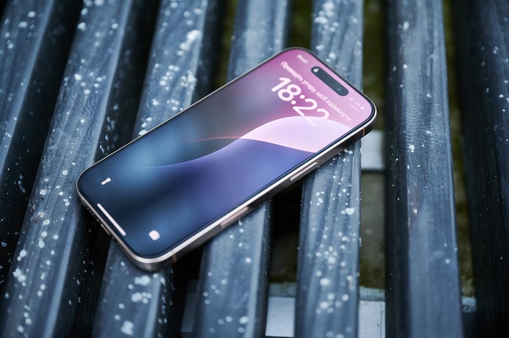 Smartphone moderno de tela grande com design elegante e display vibrante, descansando sobre uma superfície de madeira úmida, ideal para tecnologia avançada.