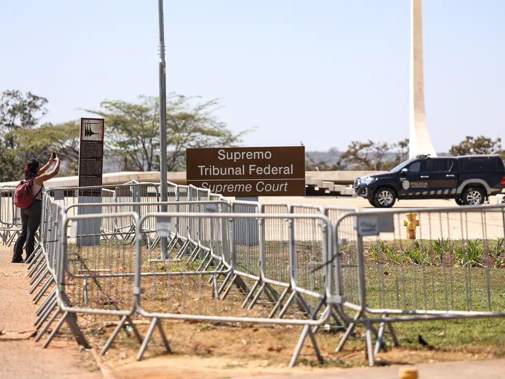 Imagem mostra pessoa tirando uma foto em frente ao prédio do Supremo Tribunal Federal com barreiras de segurança na frente, ilustrando esquema de segurança reforçado durante julgamento do Bolsonaro