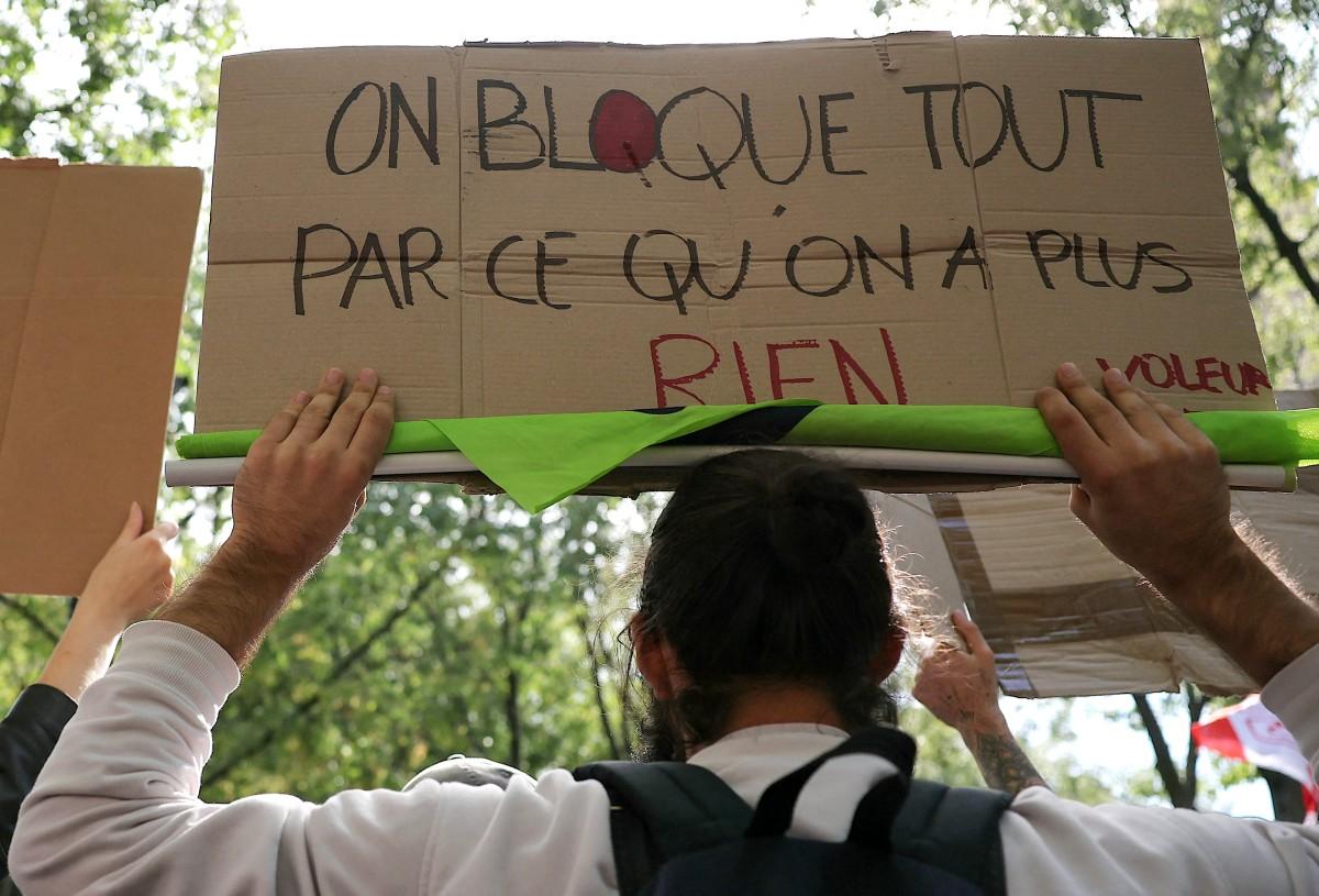 Manifestante segurando cartaz com mensagem de protesto, pedindo o bloqueio total por uma causa social: 