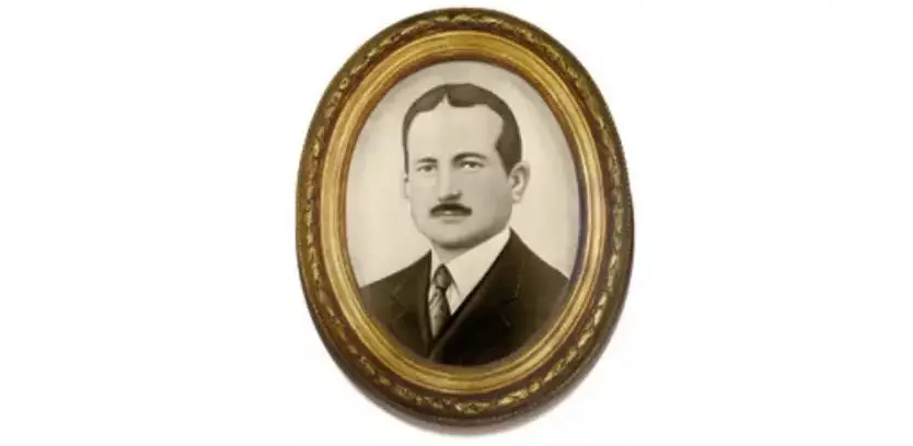 Retrato emoldurado de Álvaro Nunes Weyne, em fotografia em preto e branco, usando terno, gravata e bigode. A moldura é oval e ornamentada em tom dourado