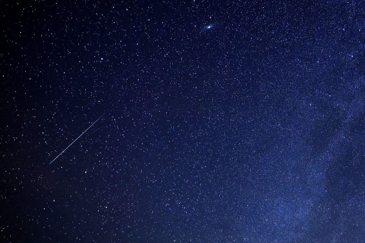 Imagem do céu noturno estrelado, com estrelas brilhando intensamente e uma estrela cadente cruzando o céu.