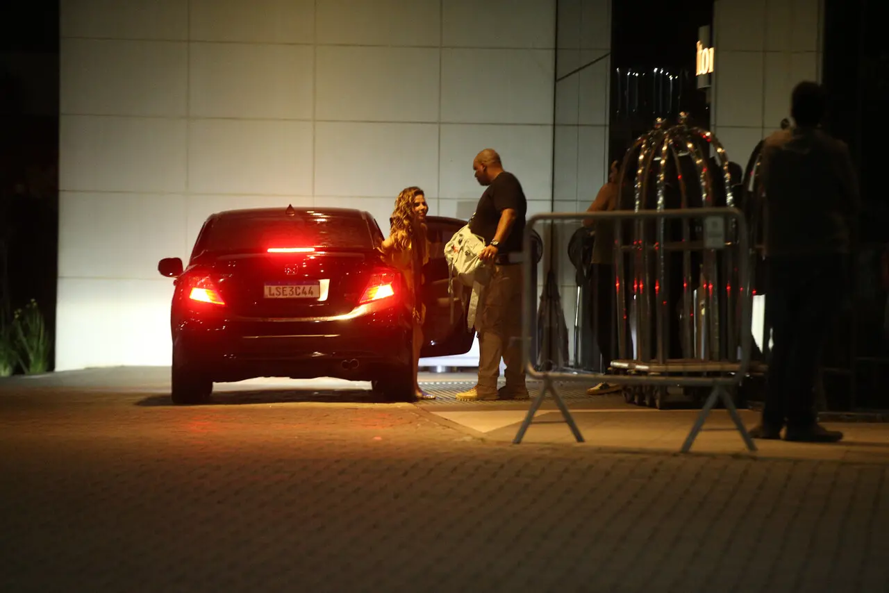 Wanessa saindo de um carro preto e uma cerca de proteção e um segurança em entrada de hotel.