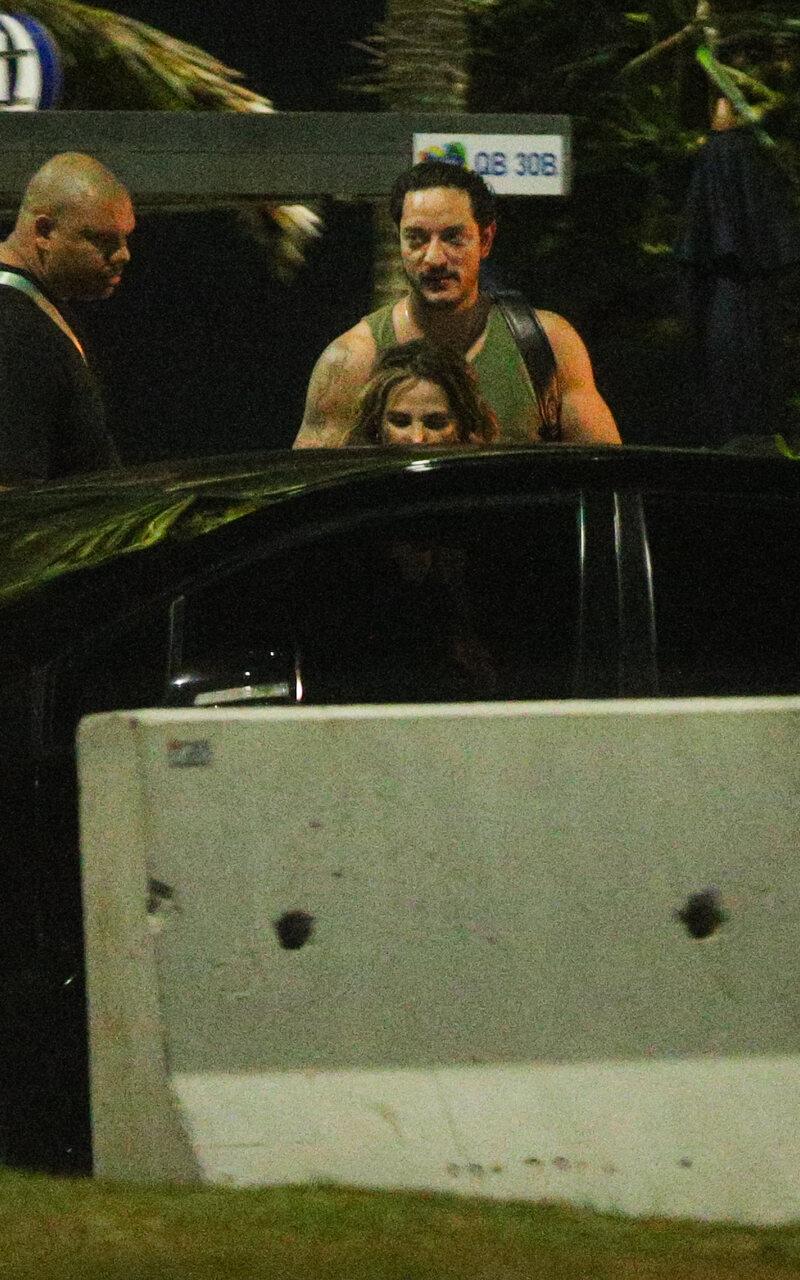 Wanessa a frente e Allan atrás, entrando em carro preto enquanto segurança observa ao lado esquerdo da foto.