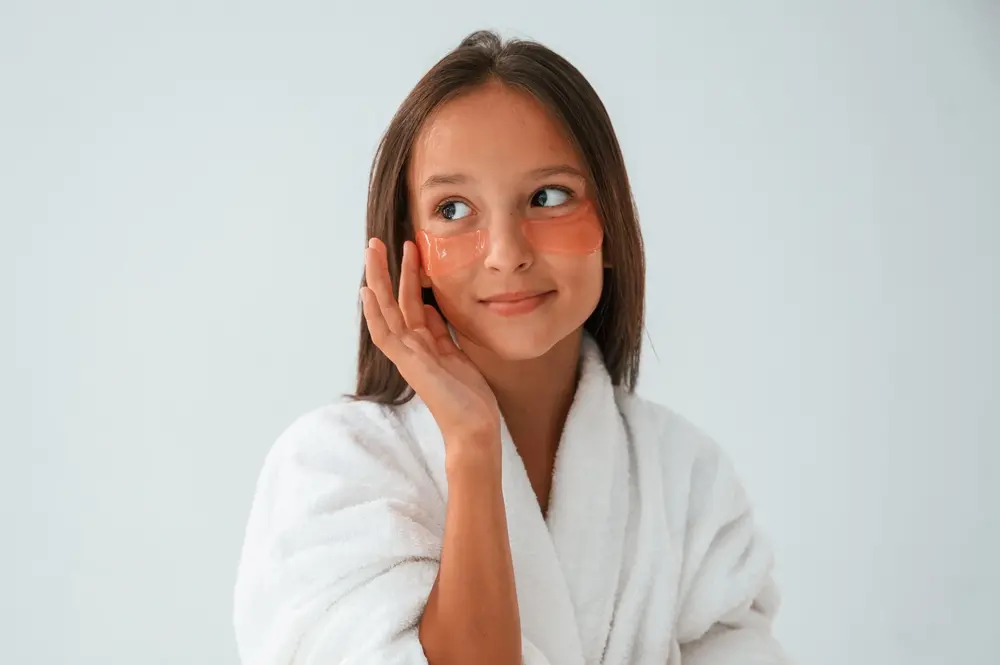 foto de criança de roupão branco fazendo skin care com máscara de olhos.