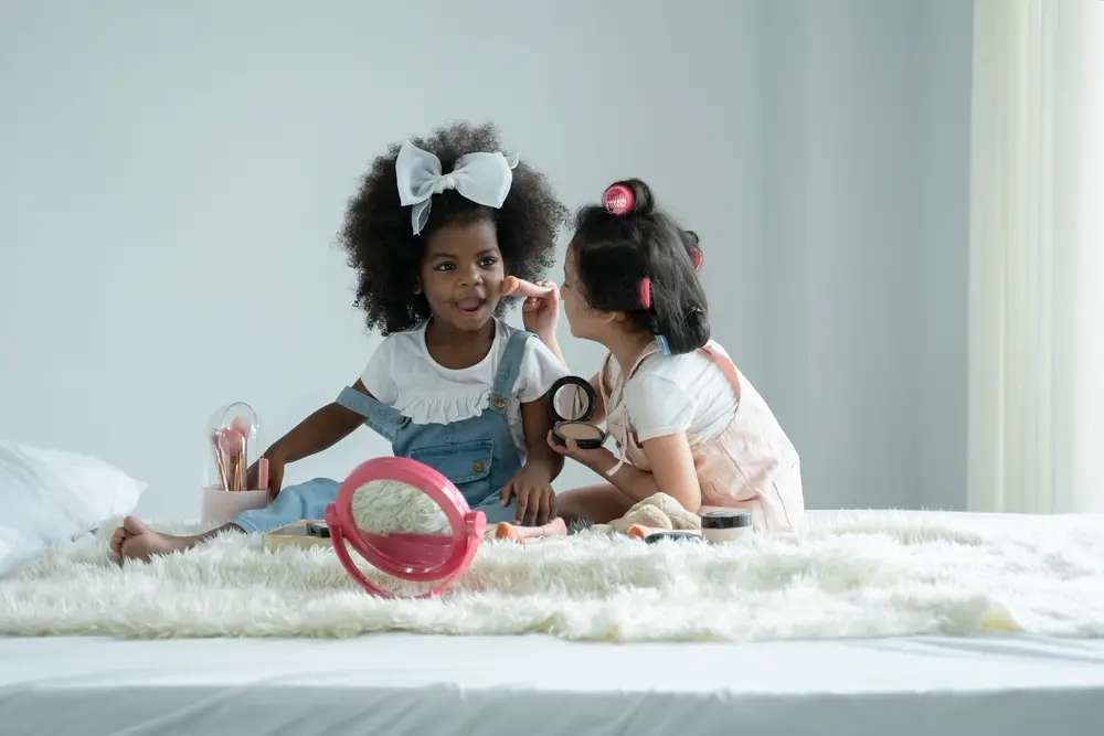 foto de crianças aplicando maquiagem uma na outra, sentadas sobre um tapete.