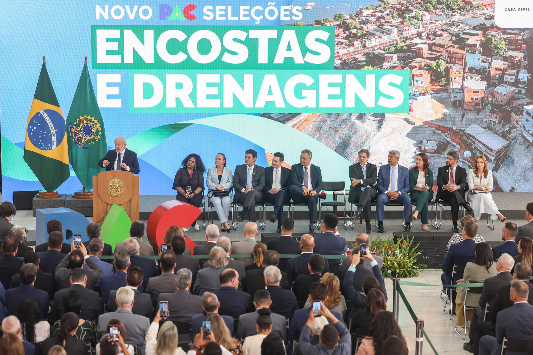 Evento no Palácio do Planalto com o presidente Lula anunciando resultados do Novo PAC Seleções, diante de autoridades e público.