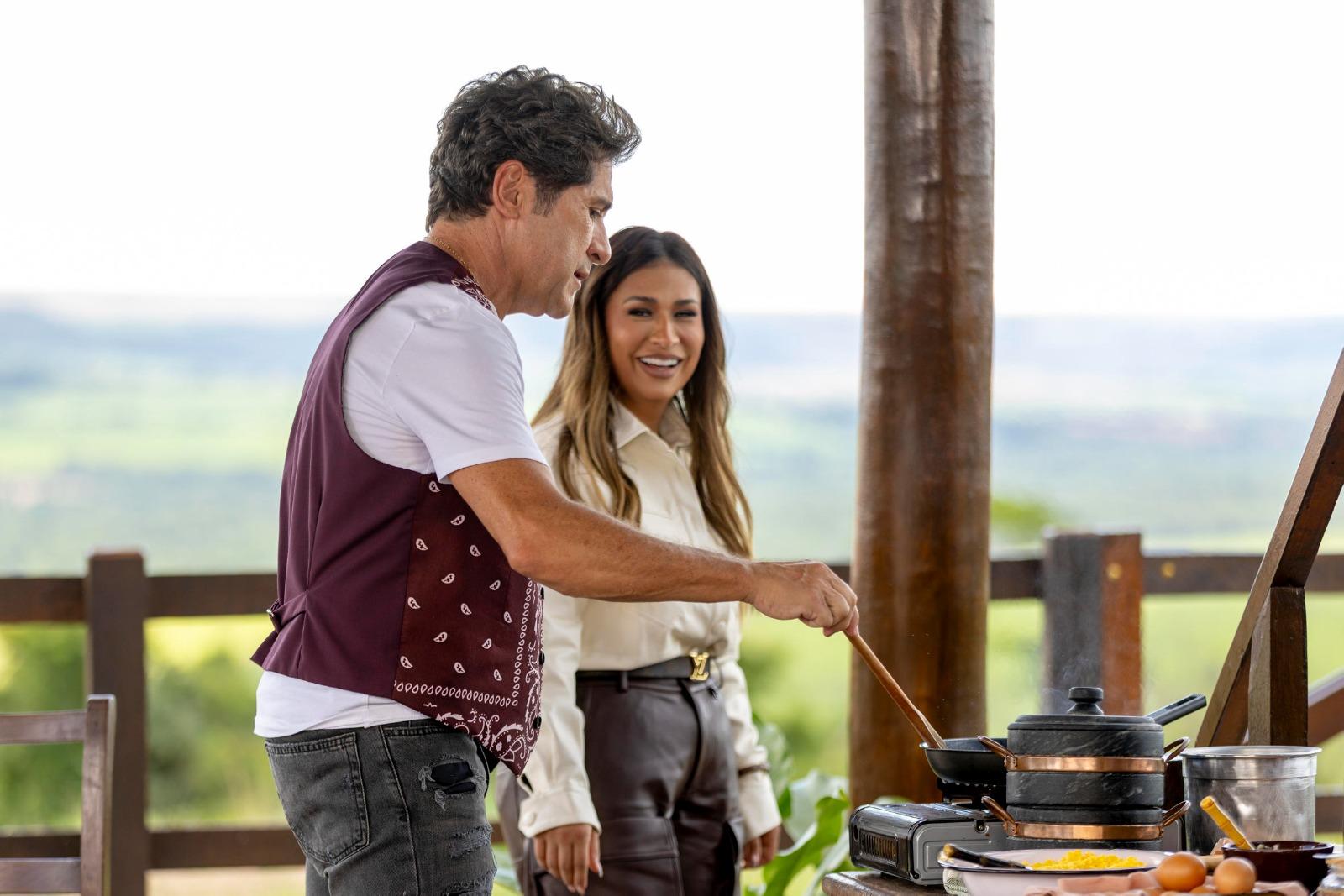 Daniel prepara uma refeição enquanto Simone observa sorrindo.