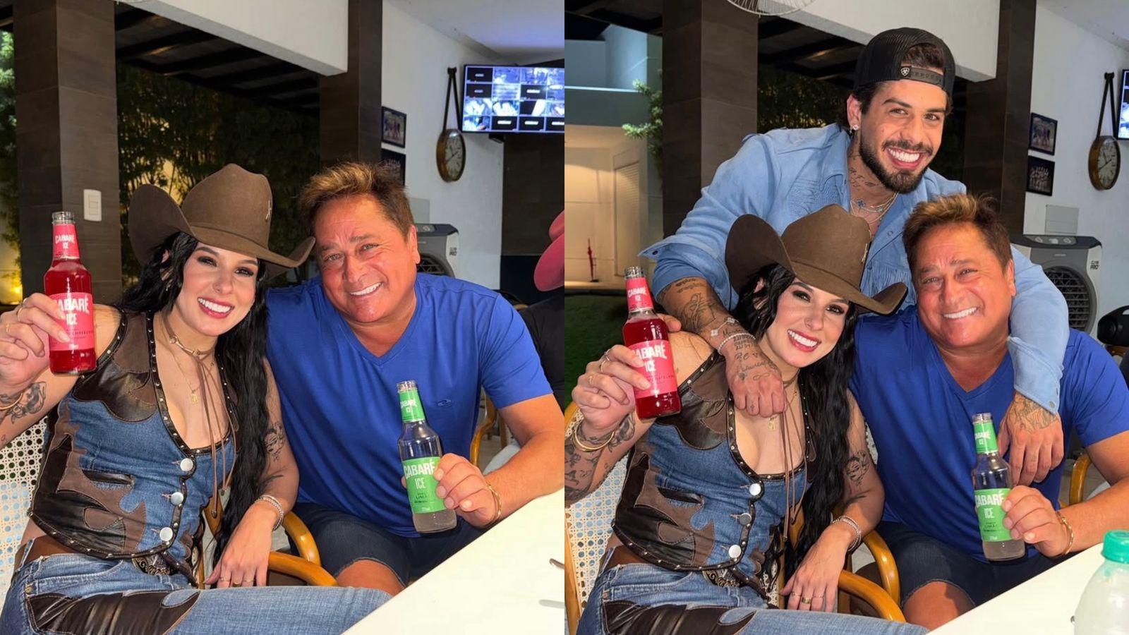 Imagem de três pessoas sorrindo e brindando com garrafas de refrigerante em um ambiente de restaurante, incluindo uma mulher com chapéu, um homem de camiseta azul e um jovem com barba e boné, em um momento de celebração.
