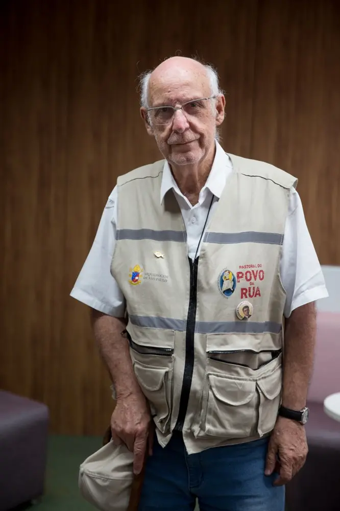 Na imagem, padre Júlio Lancellotti está em pé em uma das salas do Sistema Verdes Mares; ele traja o colete da Pastoral do Povo da Rua
