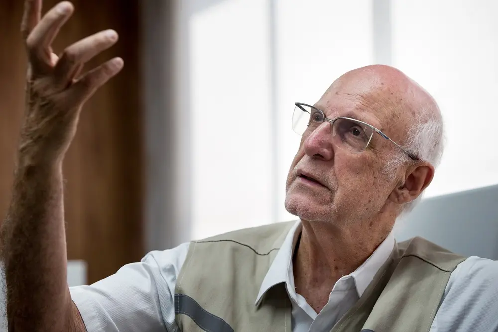 Na imagem, padre Júlio Lancellotti está sentado em sofá do Sistema Verdes Mares durante entrevista; ele traja o colete da Pastoral do Povo da Rua