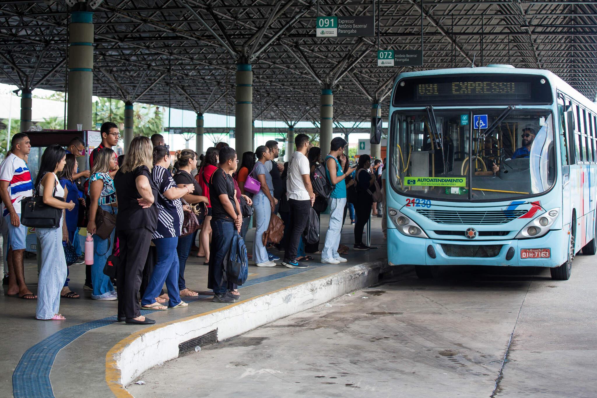 Ônibus chega a terminal, em frente à fila de passageiros.