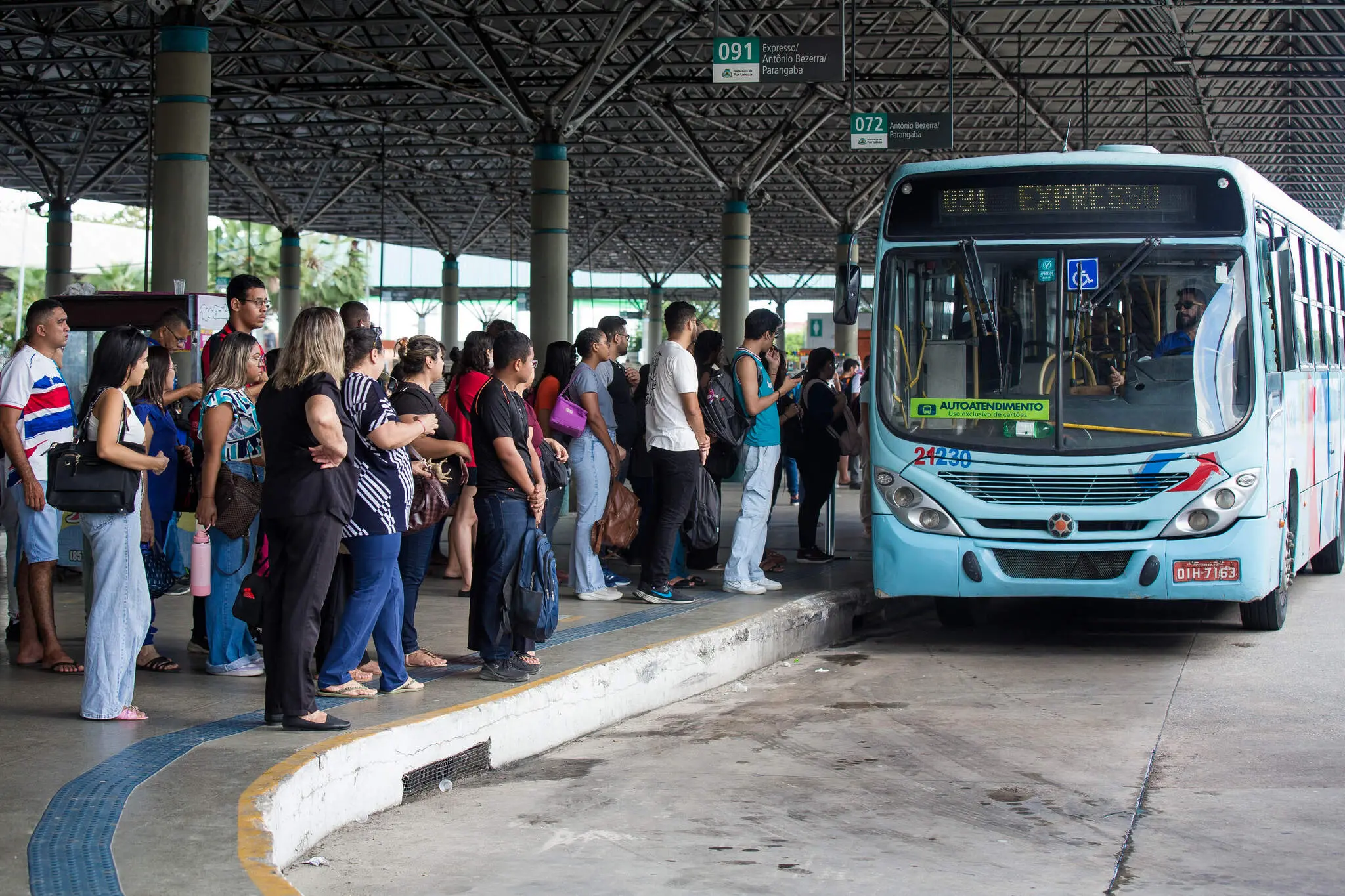 Ônibus chega a terminal, em frente à fila de passageiros.