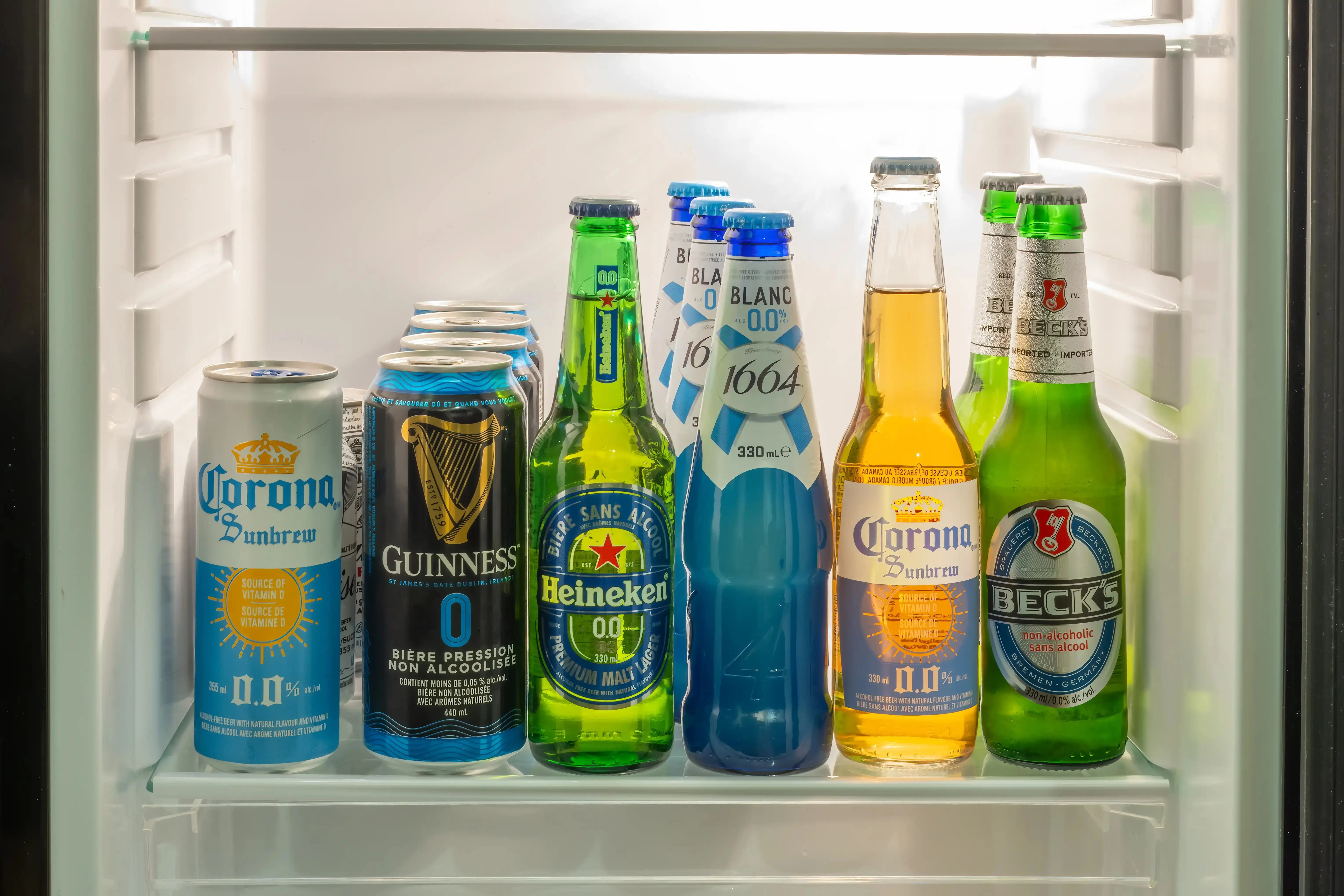 Prateleira de geladeira com diversas latas e garrafas de diferentes marcas. A variedade de opções no refrigerador levanta a questão de saúde: afinal, cerveja sem álcool faz mal ou é um bom substituto?