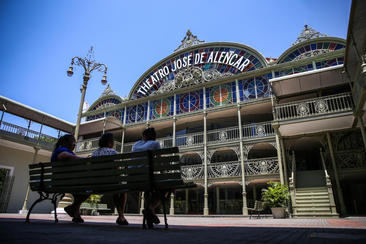 Na imagem, crianças sentadas no banco em frente à fachada do Theatro José de Alencar, Centro de Fortaleza