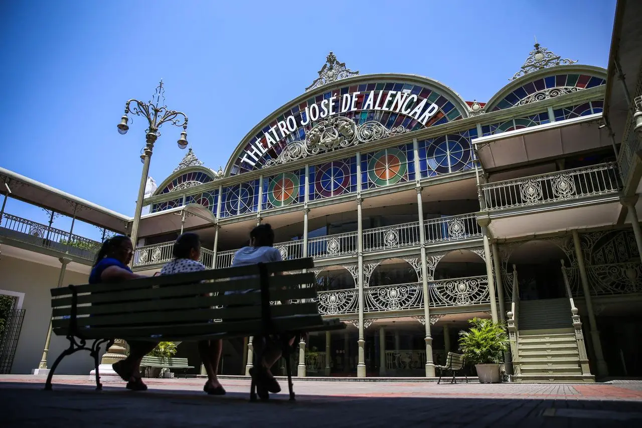 Na imagem, crianças sentadas no banco em frente à fachada do Theatro José de Alencar, Centro de Fortaleza