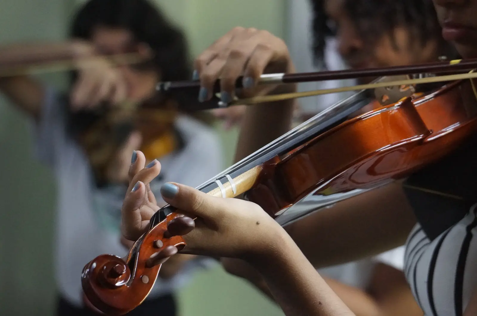 Na imagem, uma criança toca violino na escola de música Casa de Vovó Dedé; é dado um destaque especial às mãos da menina.