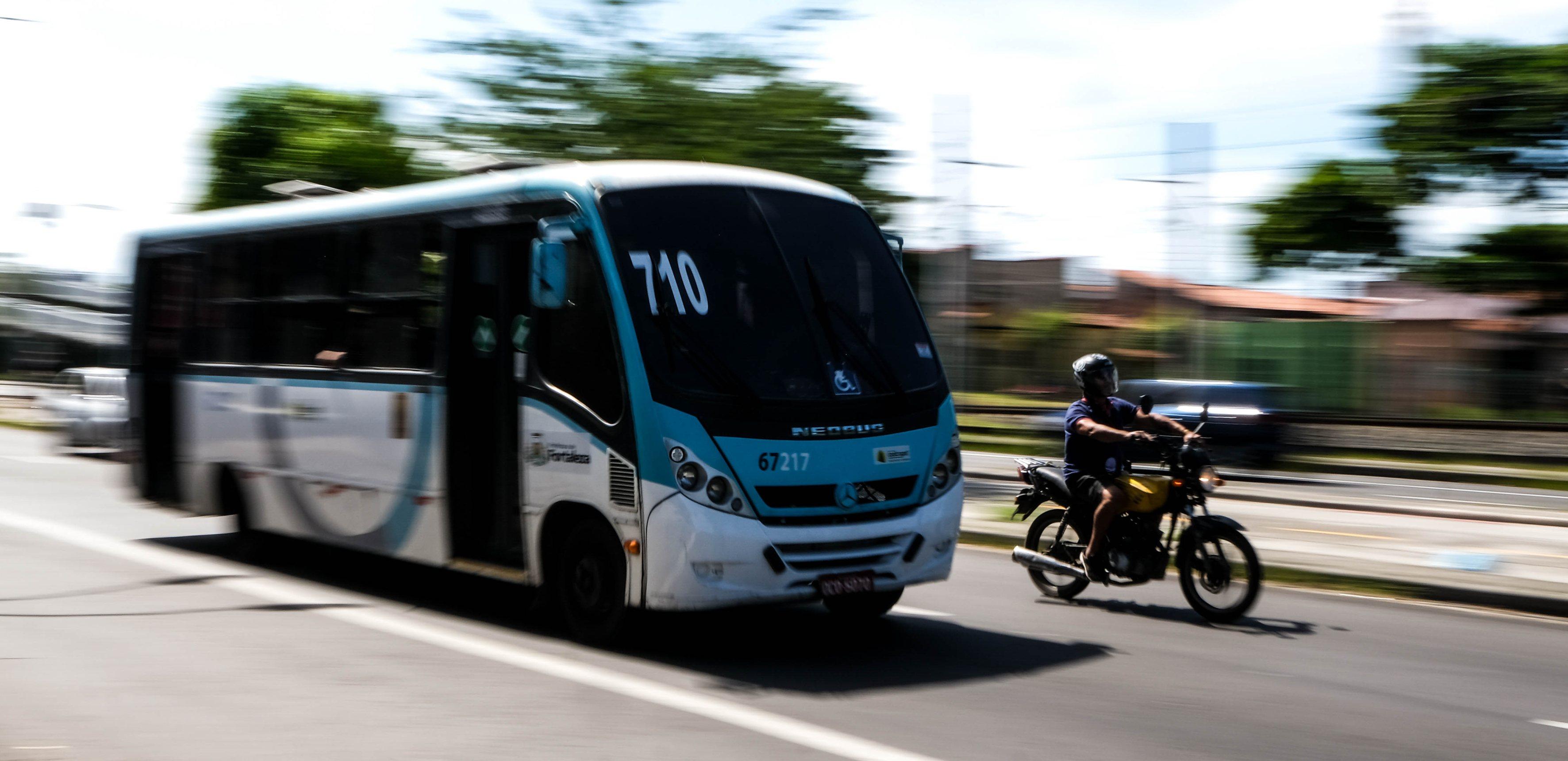 Foto de ação (panning) de um ônibus de transporte coletivo e um motociclista em movimento rápido. O ônibus tem o número da linha 710. Fundo borrado para efeito de velocidade.
