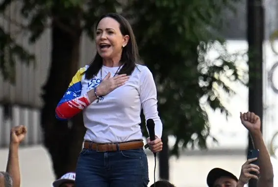 Corina Machado fala ao microfone em cima de um carro. Imagem de vencedora do prêmio Nobel que agradeceu Trump pelo apoio.