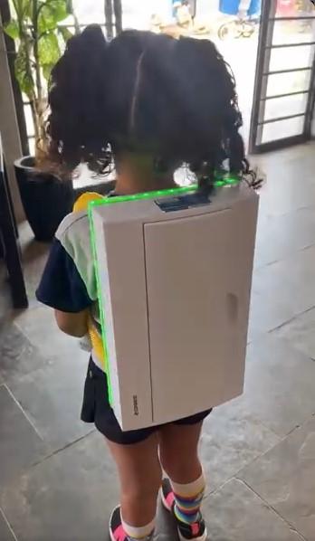 Foto da menina Sofia, acompanhada de uma mochila que simula uma caixa de energia