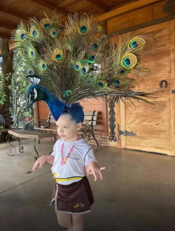 Foto da menina Donata, que foi para o colégio com um pavão de mentira, criado pela mãe, em seu cabelo