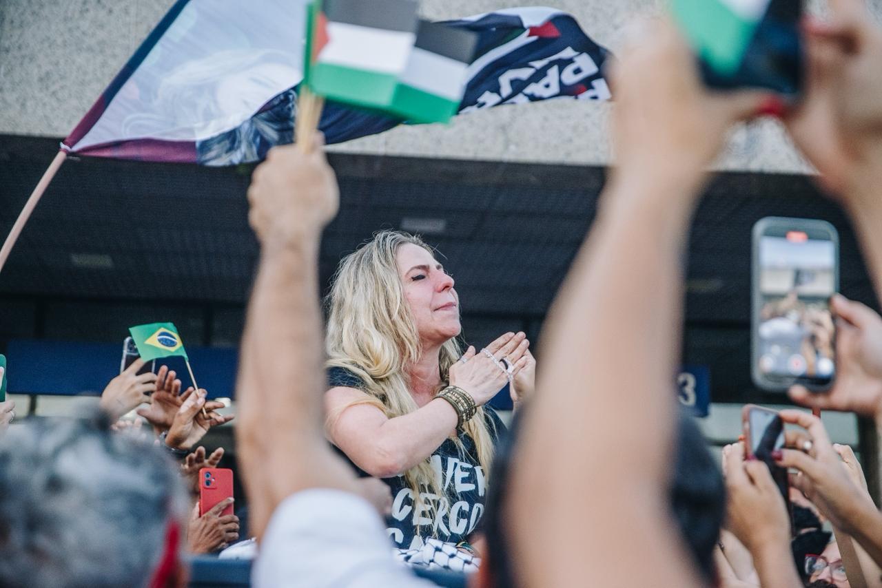 Registro da deputada federal Luizianne Lins ao voltar a Fortaleza após ser detida em Israel; a parlamentar aparece emocionada e é possível ver celulares e bandeiras do Brasil e da Palestina.