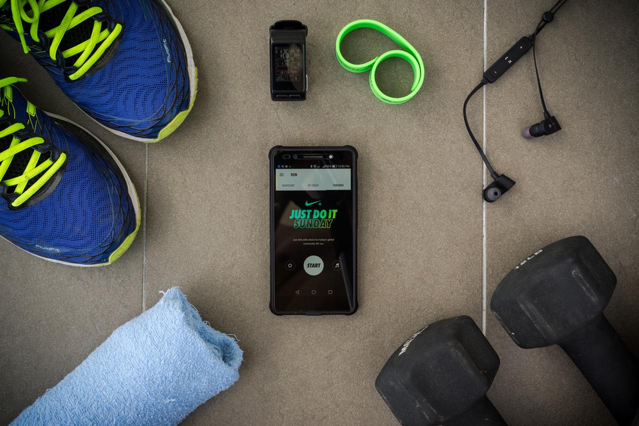 Nike Training Club em um celular ao lado de celular e pesos de academia