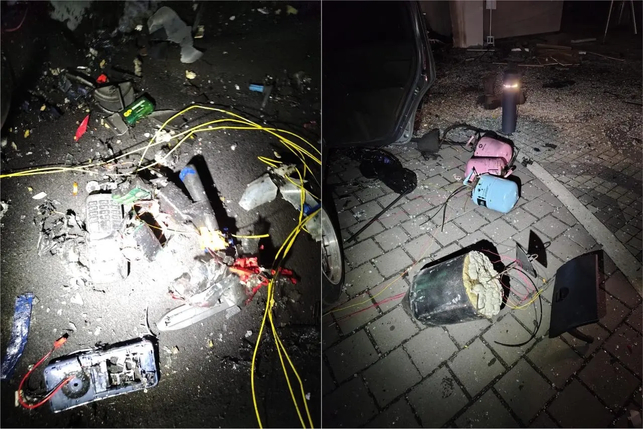 Imagem de uma cena de acidente envolvendo eletrônicos danificados, cabos espalhados e objetos destruídos na rua durante a noite. bombas