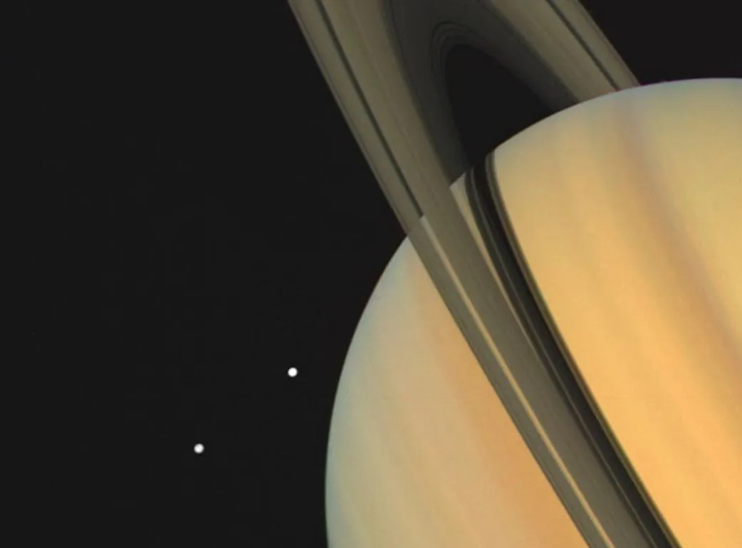 Os satélites Tétis e Dione, que não fazem parte diretamente do sistema de anéis de Saturno. Entretanto, a gravidade dessas luas geladas influencia e interage com as partículas de gelo e rocha que compõem os anéis, moldando sua estrutura.