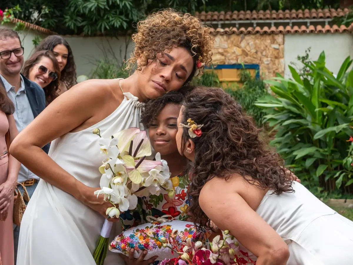 Foto de Laís e Cecília se casando. Na foto, Cecília beija o rosto da filha Sarita. Todas seguram buquês.
