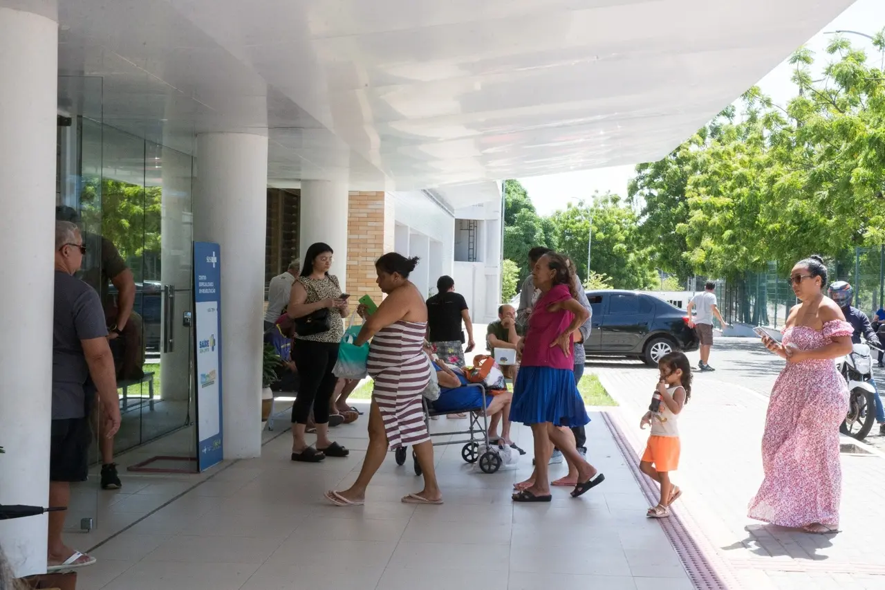 Pessoas andando na frente da recepção de policlínica no bairro Passaré, em Fortaleza.