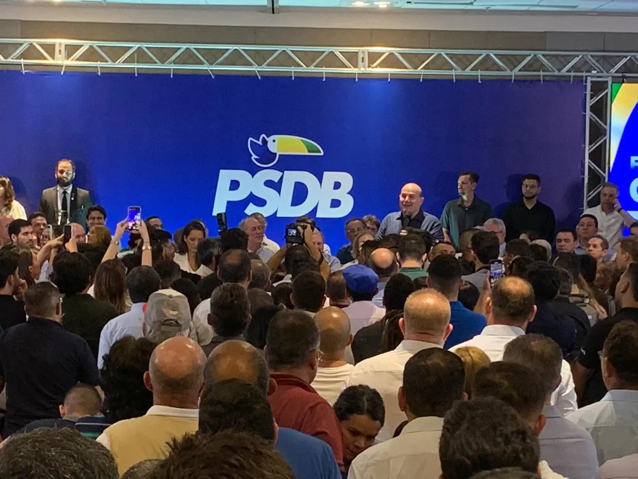 Auditório lotado, com logomarca do PSDB no fundo, à frente Roberto Cláudio faz discurso