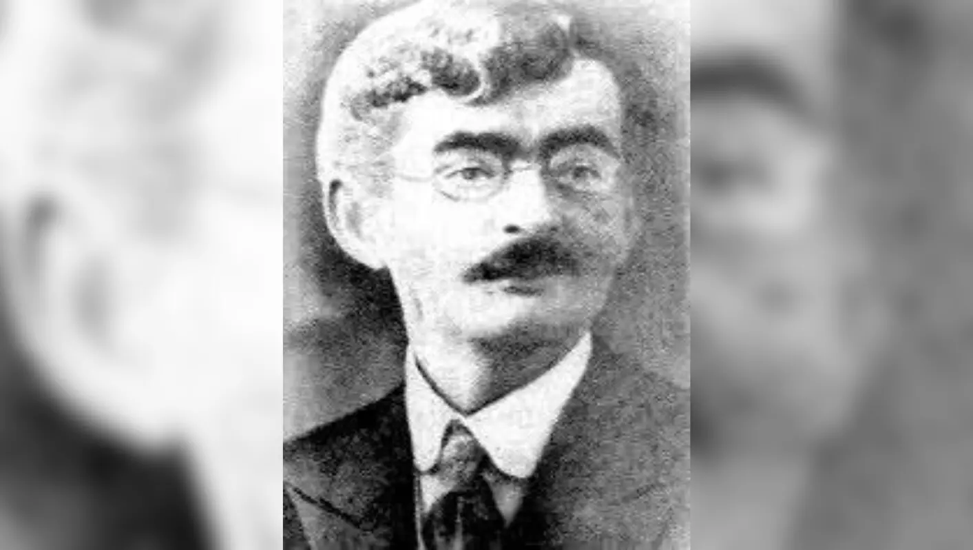 Em foto preto e branco, Quintino Cunha posa olhando para o horizonte. Ele veste um paletó e usa um óculos arredondado