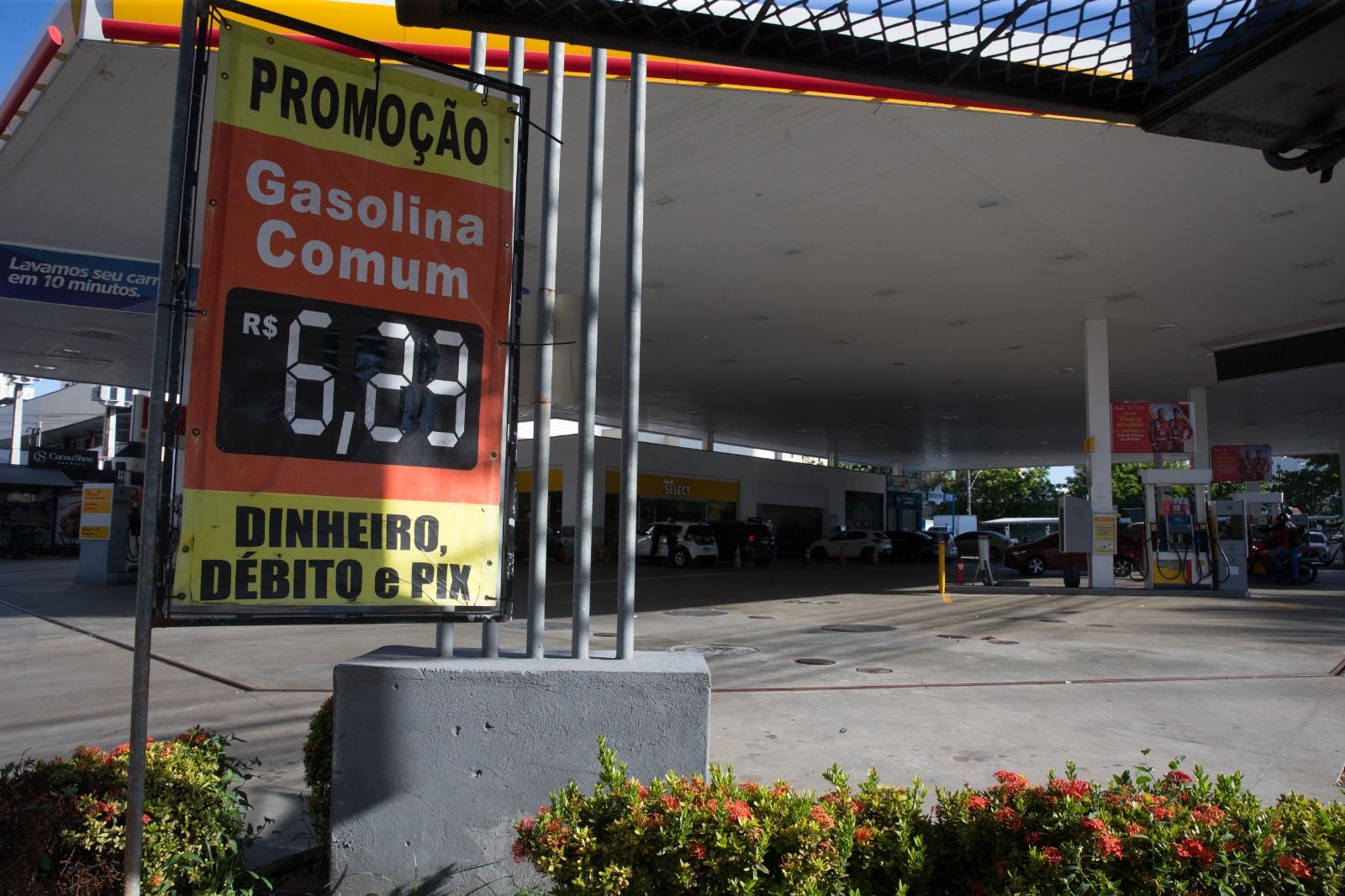 A imagem mostra um posto de combustíveis da rede Shell, em Fortaleza, com uma placa destacando o preço da gasolina comum a R$ 6,23, para pagamento em dinheiro, débito ou Pix. O anúncio indica “promoção”, enquanto veículos são vistos abastecendo no fundo.
