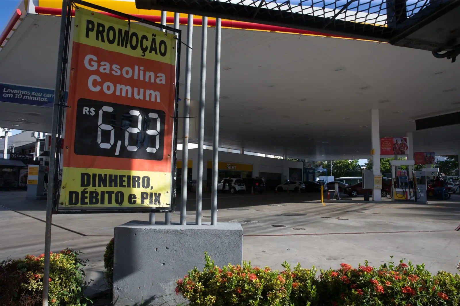 A imagem mostra um posto de combustíveis da rede Shell, em Fortaleza, com uma placa destacando o preço da gasolina comum a R$ 6,23, para pagamento em dinheiro, débito ou Pix. O anúncio indica “promoção”, enquanto veículos são vistos abastecendo no fundo.